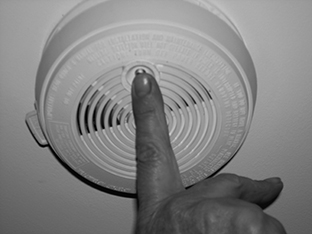 Finger pressing the test button on a smoke alarm